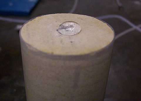 Photograph of a core after treatment with surfactant F, indicating change in wettability of the surface. The drop of brine does not imbibe spontaneously into the carbonate rock.