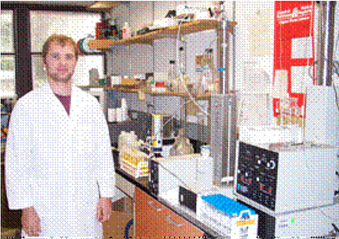 Researcher stands next to equipment to determine surfactant concentration of injection fluid before and after contact porous media.