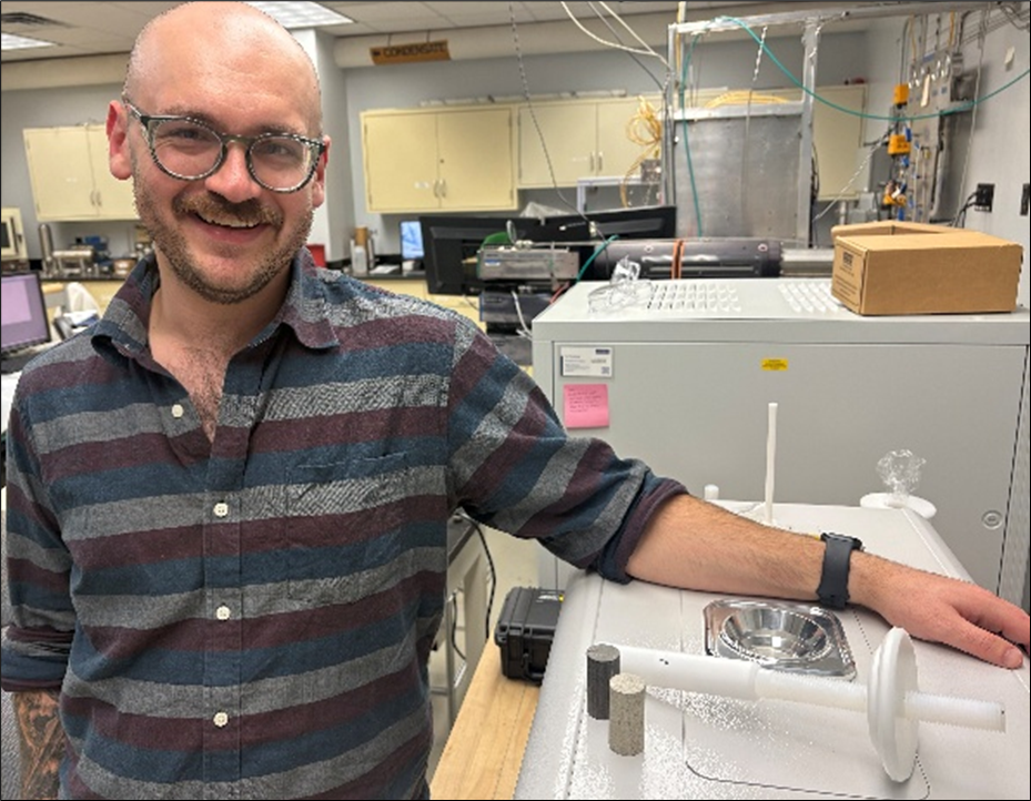 NETL researcher Matthew Grindle poses with rock cores and the Lab’s nuclear magnetic resonance (NMR) spectroscopy unit.